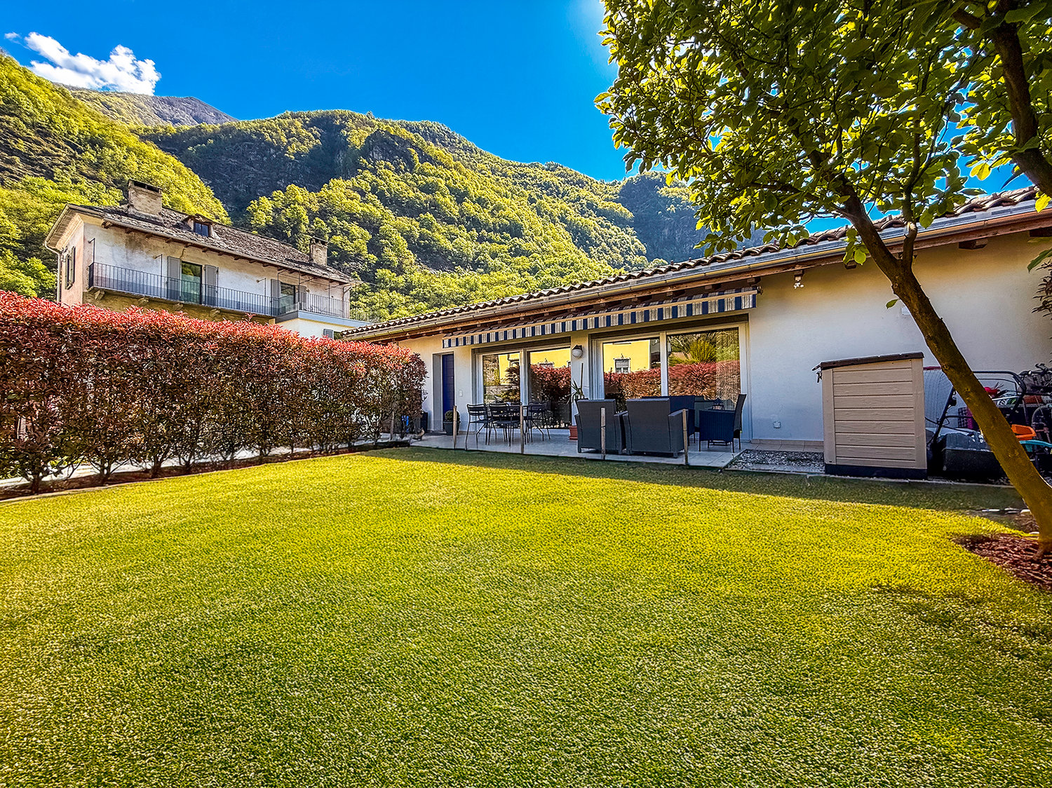 Two houses, with white walls, green lawn, mountain in the background
