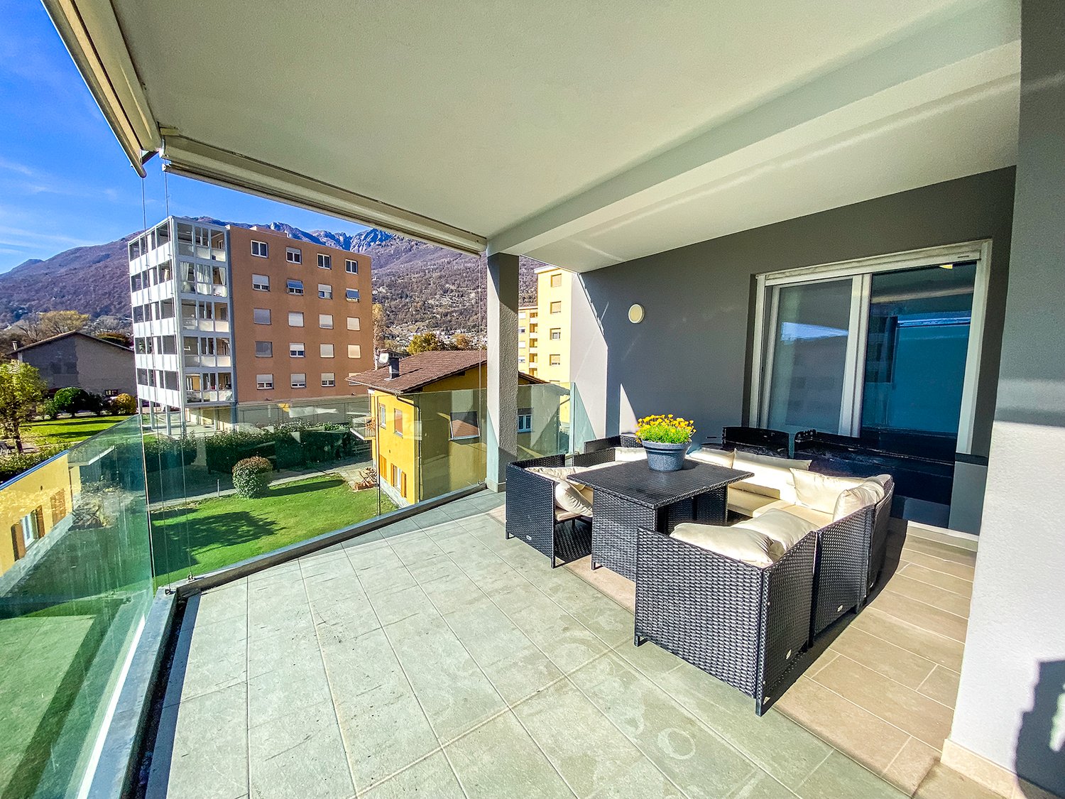 Balcony with glass railings, wooden furniture, potted plant, tiled floor, green lawn view