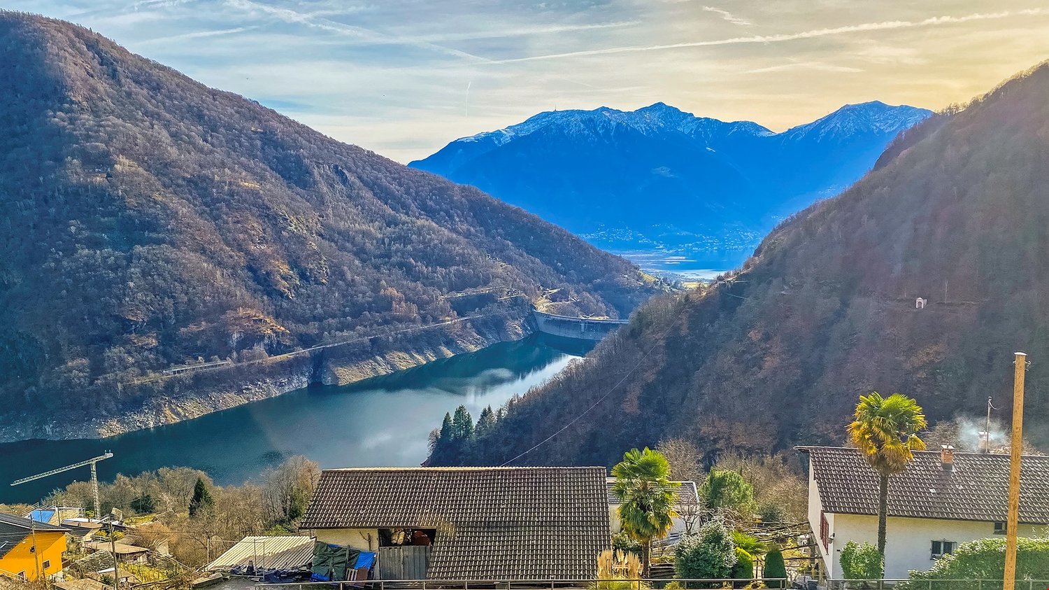 lake nestled between the mountains, residential houses with tiled roofs, dam on the lake, trees and shrubs