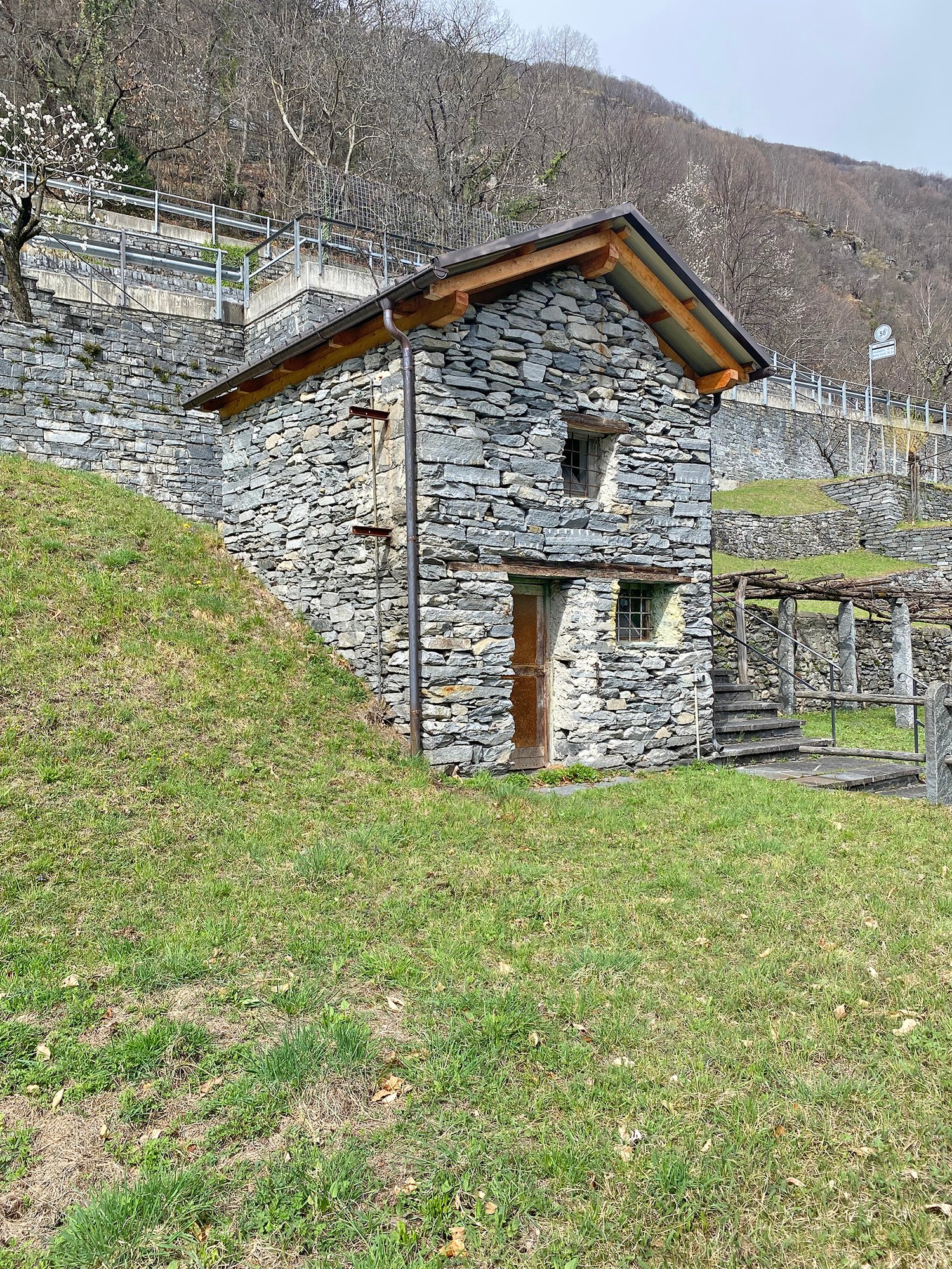 Stone house, wooden roof, wooden door, two windows, located on a slope