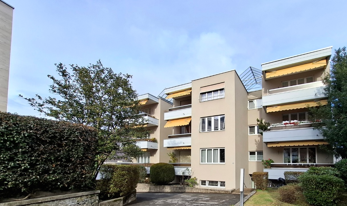 4 story building, beige exterior, multiple balconies, awnings, greenery