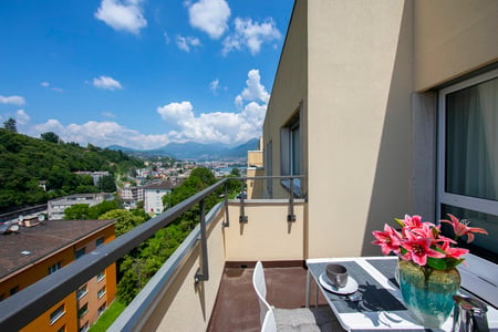 Table with vase of pink flowers, white chairs, balcony with city view
