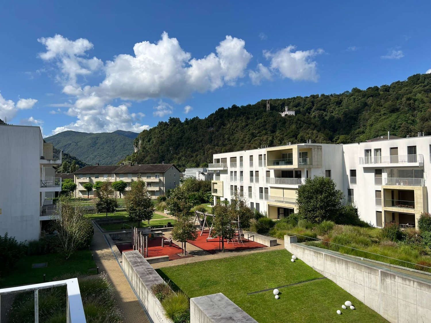 Outdoor area with apartment buildings, playground, and mountains in the background.
