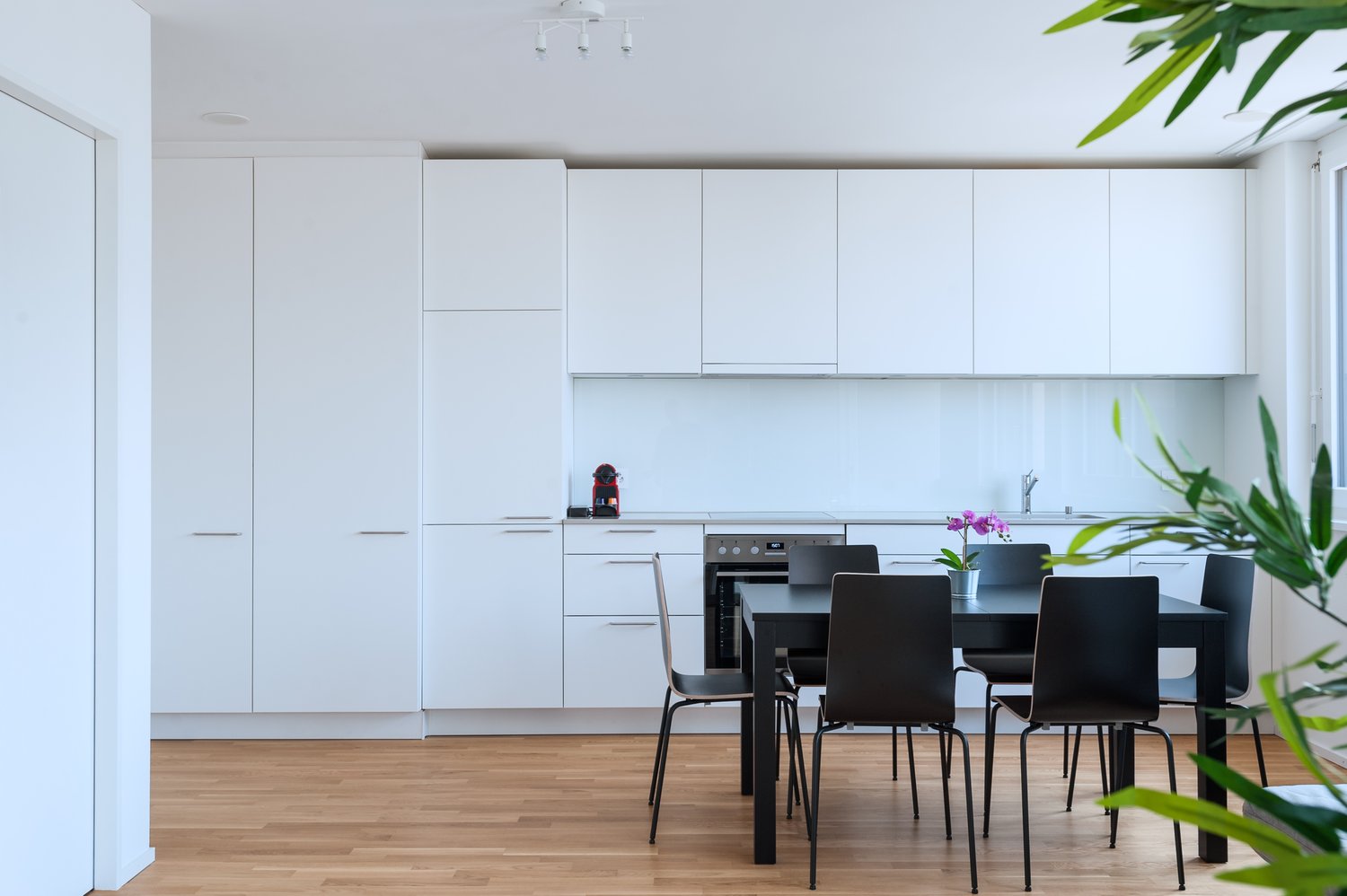 Spacious, modern kitchen with white cabinets, stainless steel appliances, and a dining table with black chairs. The kitchen has a minimalist, clean design with plenty of storage space.