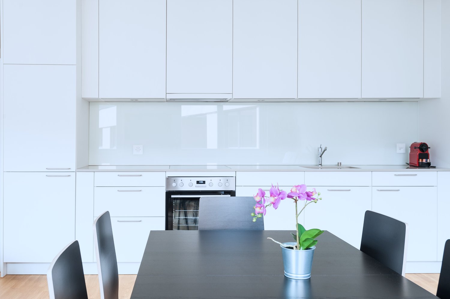 Modern white kitchen with black countertop, built-in oven, and orchid plant on the dining table