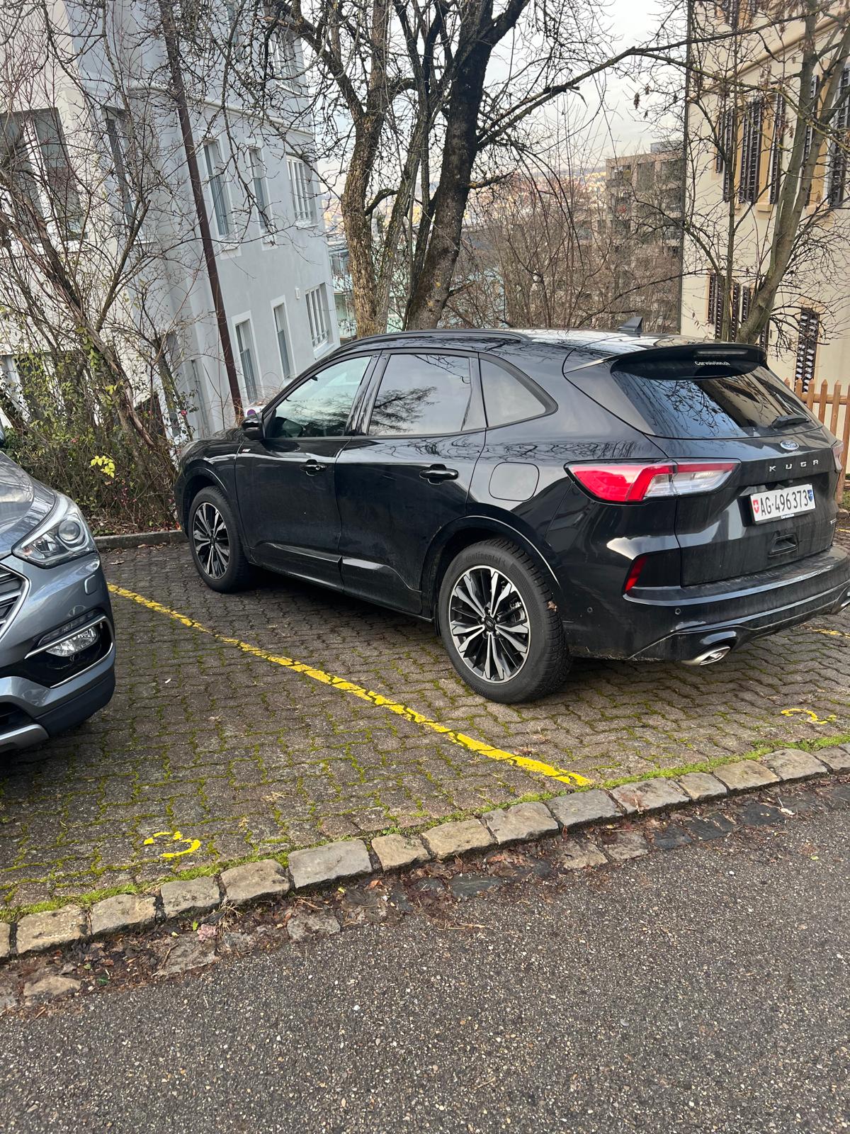 Black Kia Sorento SUV parked on the street, with a grey car parked next to it. The SUV has a rear spoiler and large wheels.