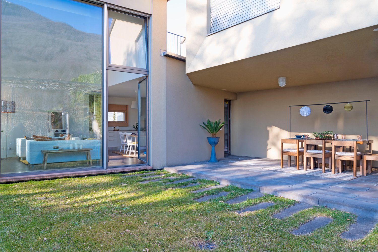 modern house, large glass windows, outdoor dining area, potted plant, grassy lawn