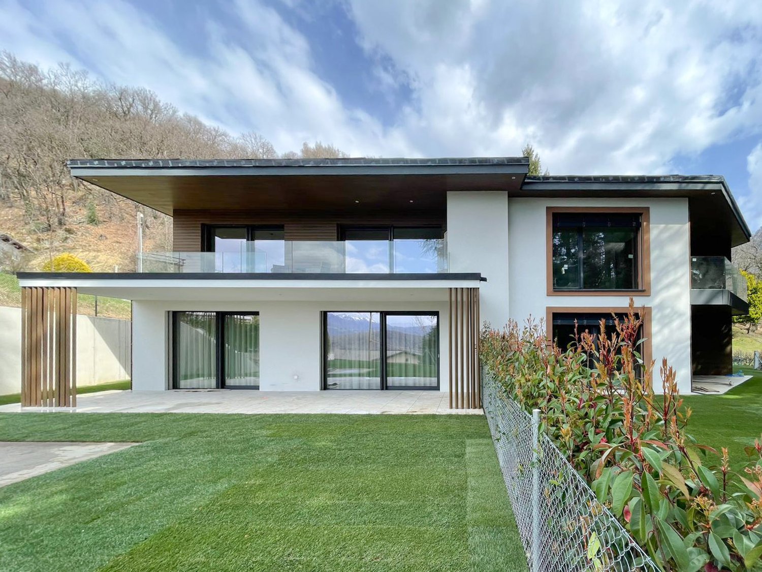 Modern house, white exterior, large glass windows, balcony, wooden fence, well-maintained lawn