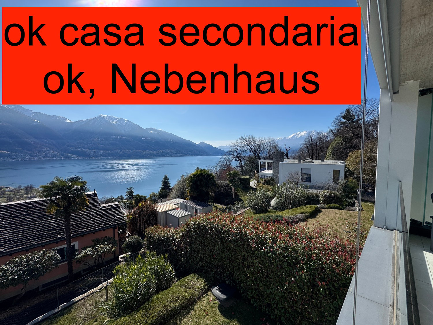 House with a view of a lake and mountains, surrounded by a garden with bushes and trees