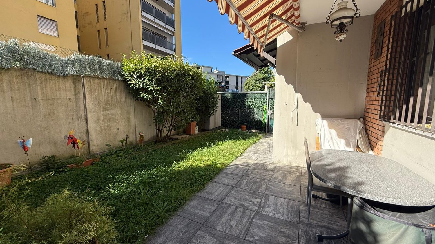 small patio with plants, trees, and grass, table and chairs