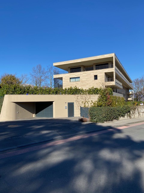 Modern architectural design, beige exterior, multiple levels, garage entrance, greenery on the roof, clear blue sky