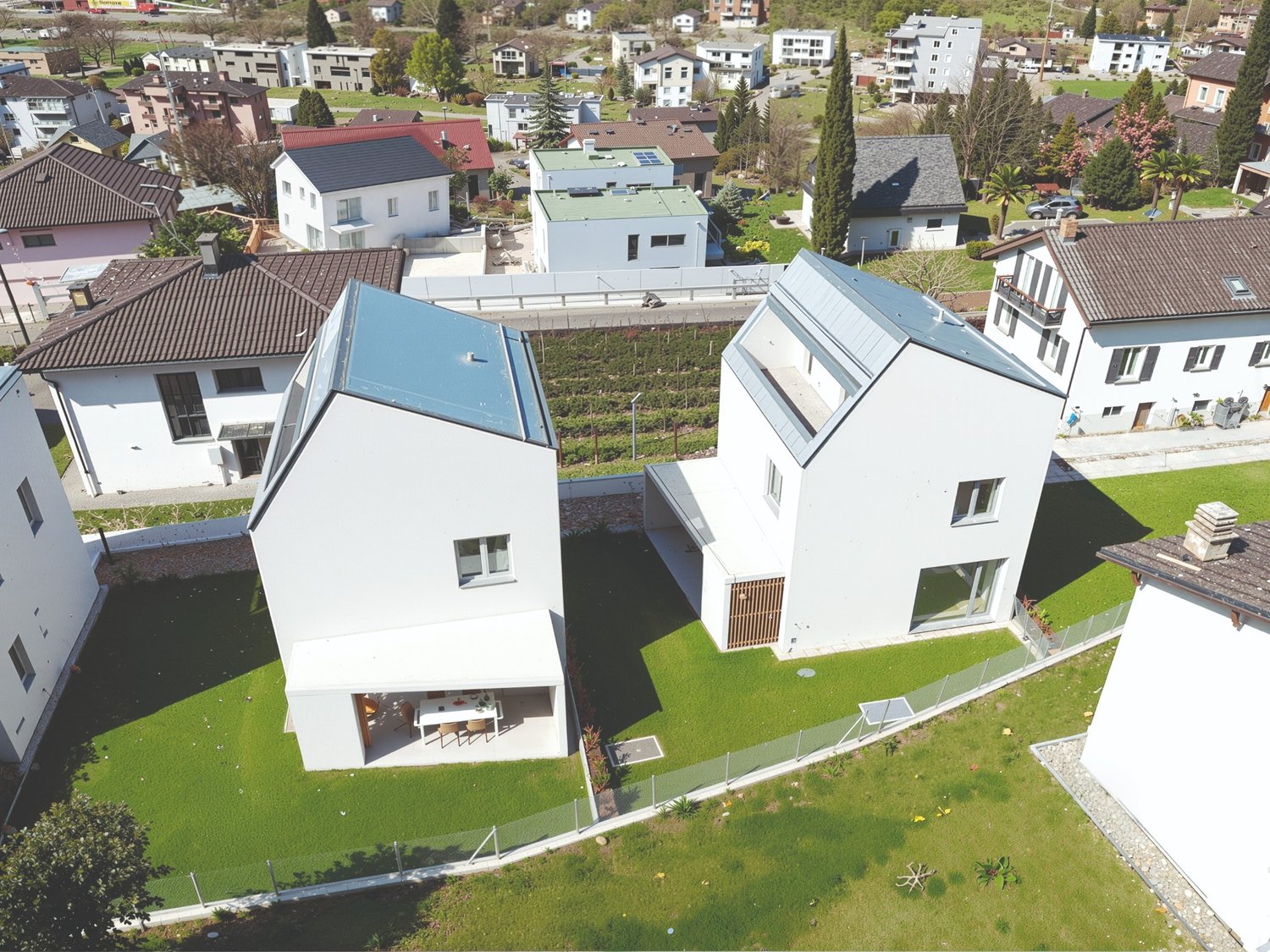 Modern white houses with solar panels on the roof, surrounded by a green lawn and a fence, aerial view