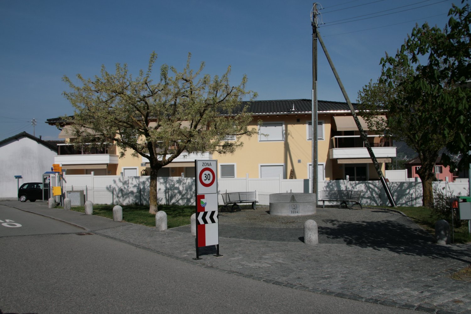 Yellow building with white fence, trees, benches, and a speed limit sign