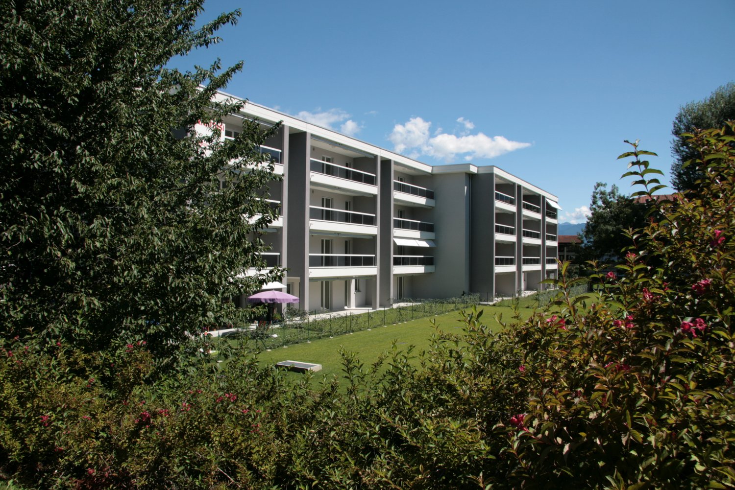 Modern apartment building with multiple floors, balconies, and a well-maintained garden area.