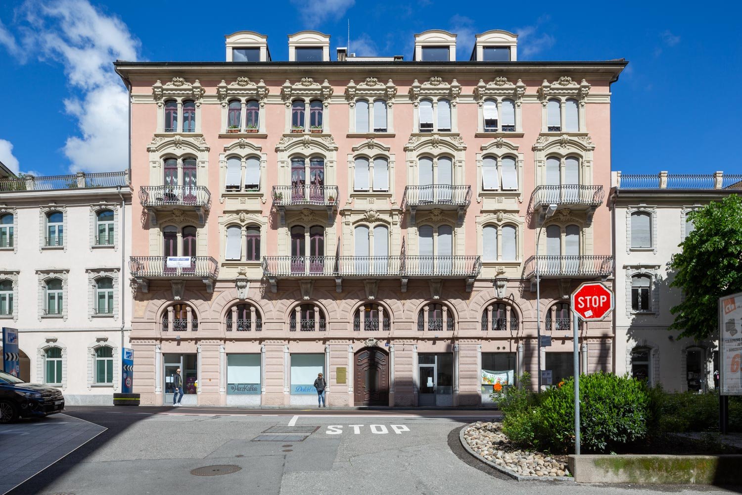 Large building with arched windows, decorative balconies, arched entryway, multiple floors, pink exterior, arched doors, central courtyard area
