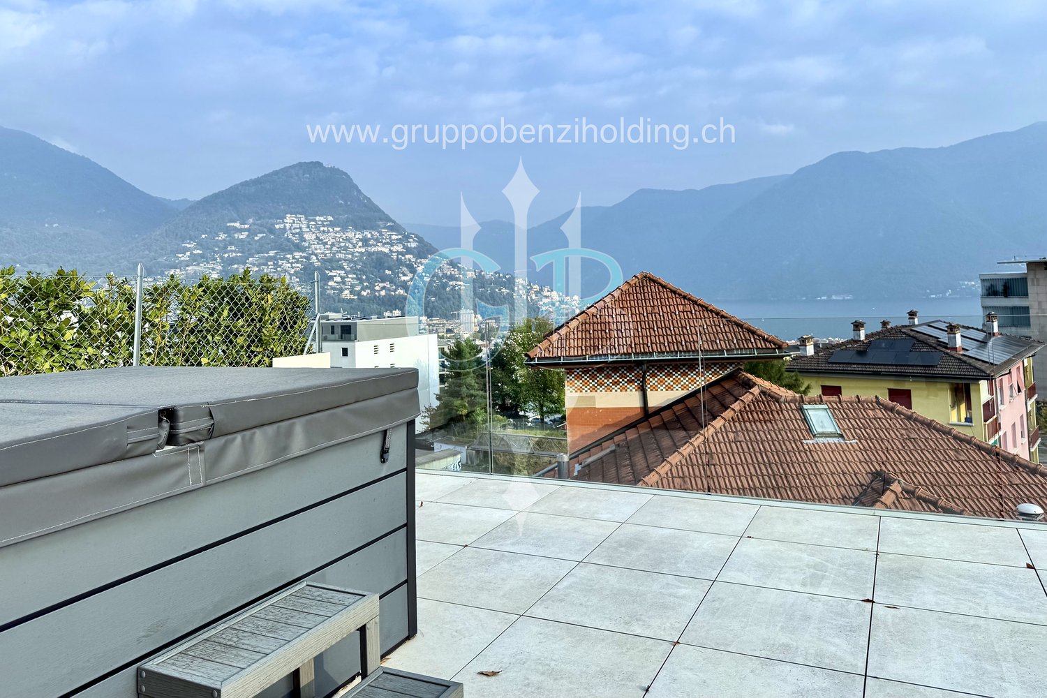 Terrace with tile floor, covered spa, houses in the background, glass railing, mountains in the distance