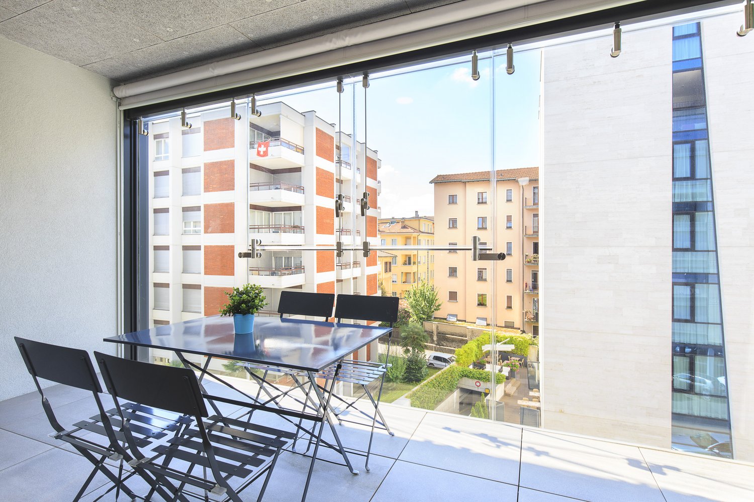 modern furnished balcony, large windows, view of other buildings, outdoor dining table and chairs