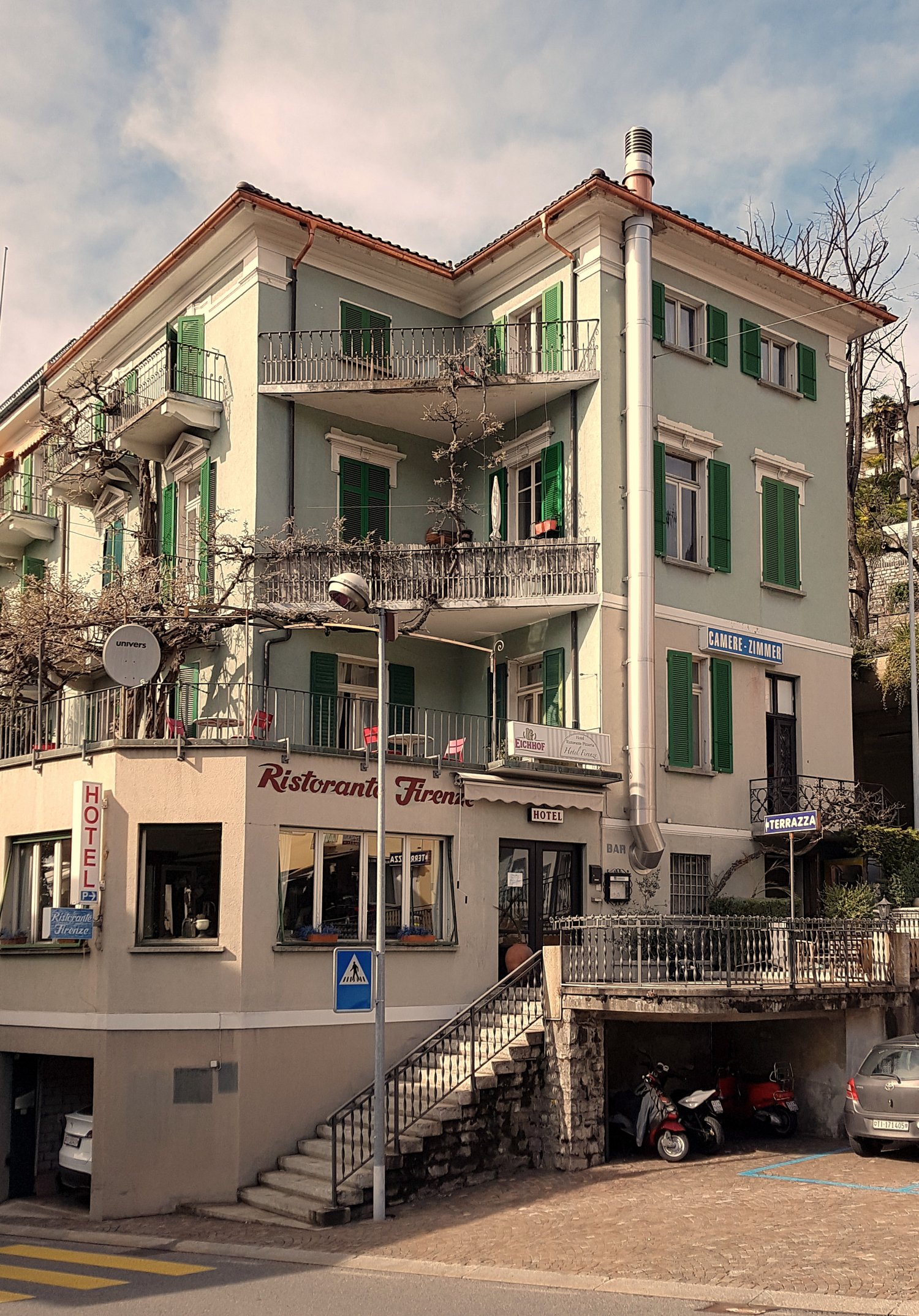 3-story building, white exterior, green shutters, balcony on first and second floor, awnings, restaurant on the ground floor, garage entrance