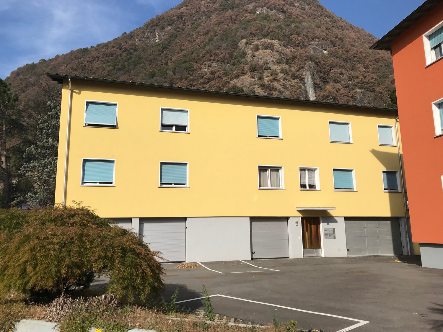 3 story yellow house, three garages in front, parking lot, mountain in the background