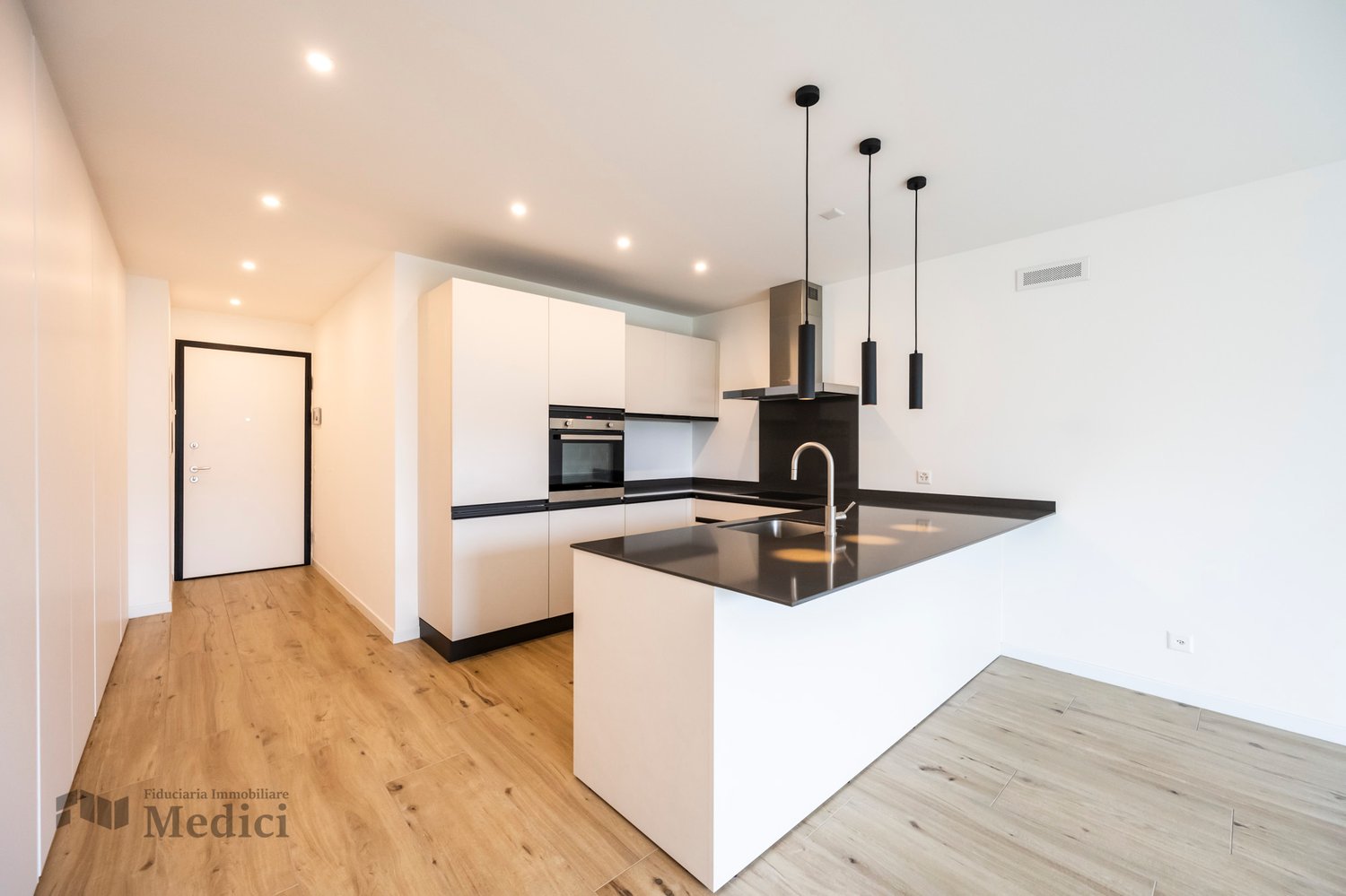 Empty modern kitchen with white cabinets, black countertops, wooden floor, oven, dishwasher, and sink with faucet.