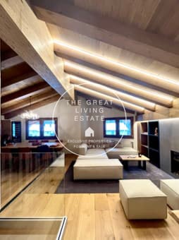 Spacious living room with high vaulted ceilings, exposed wooden beams, large windows providing natural light, hardwood flooring, and a cozy seating area with sofas and ottomans.
