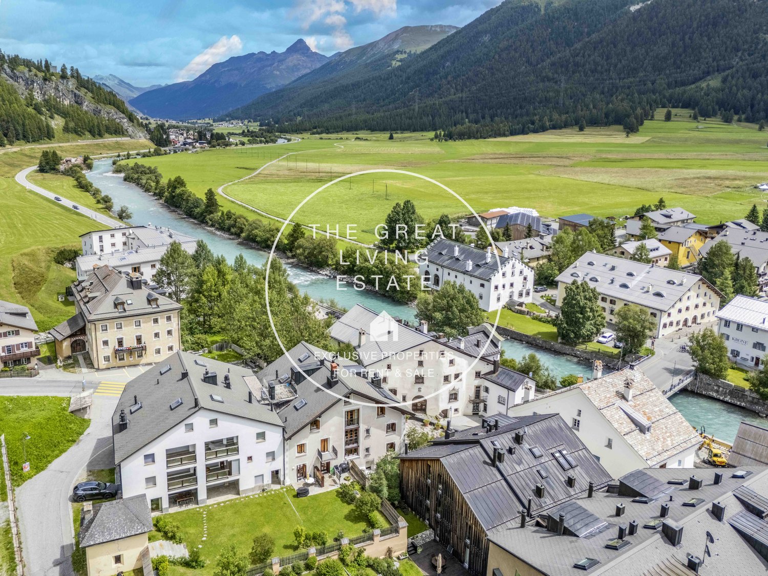 multi-story buildings, river, mountain landscape, surrounded by trees and greenery, flat roofs, gardens and driveways, yellow machinery in the river