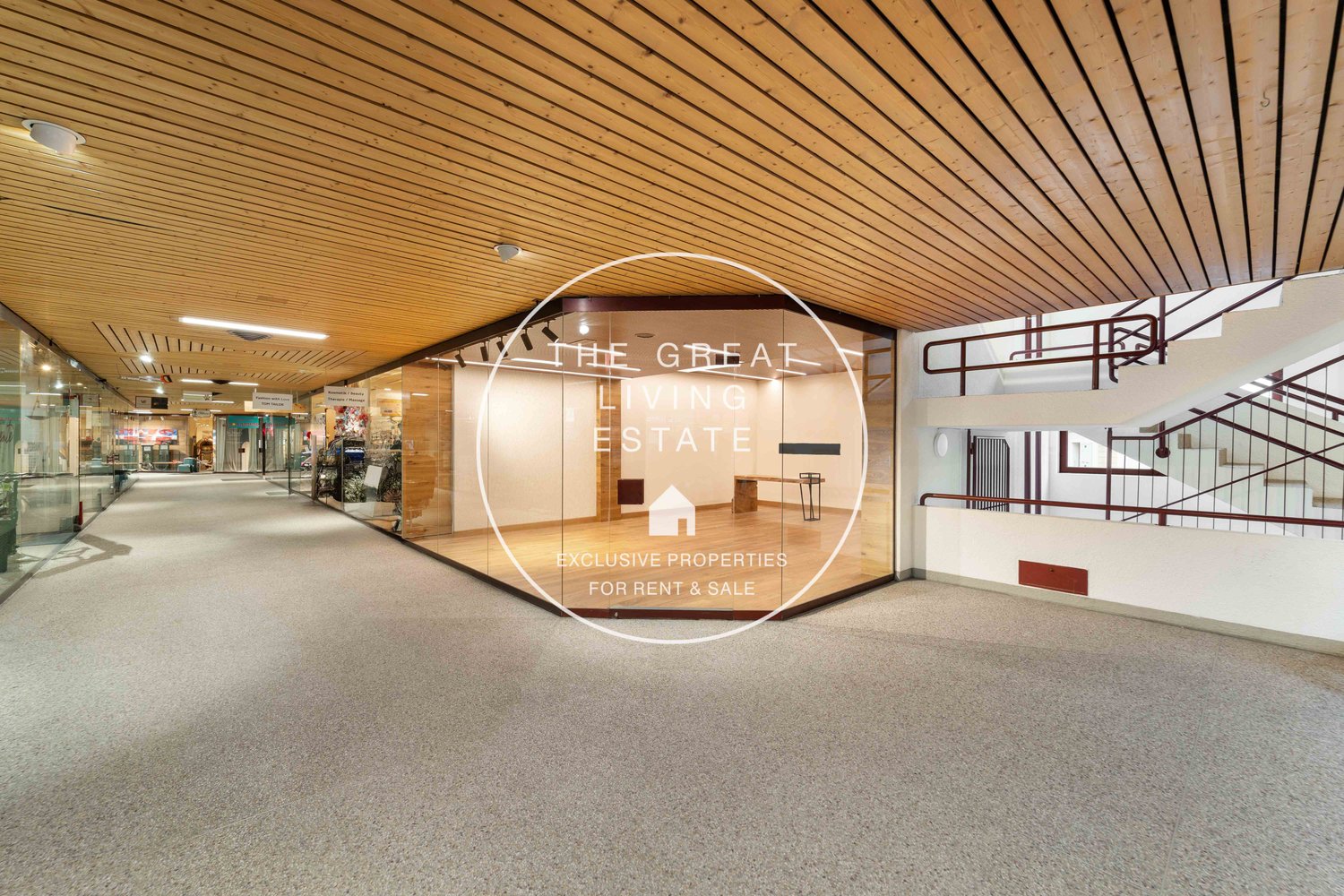 Open corridor with carpeted floor, glass walls, stairs, and a sign about renting and selling properties.