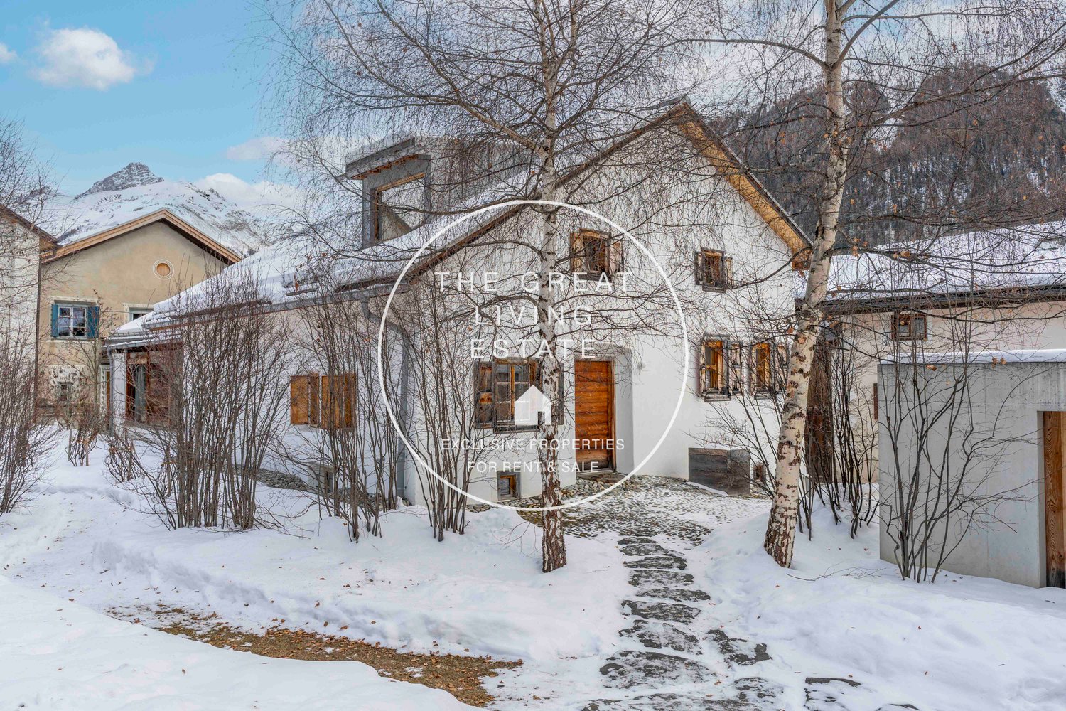 Snow-covered exterior, rustic design, wooden doors, snow-covered roofs, surrounded by trees, mountains in the background.