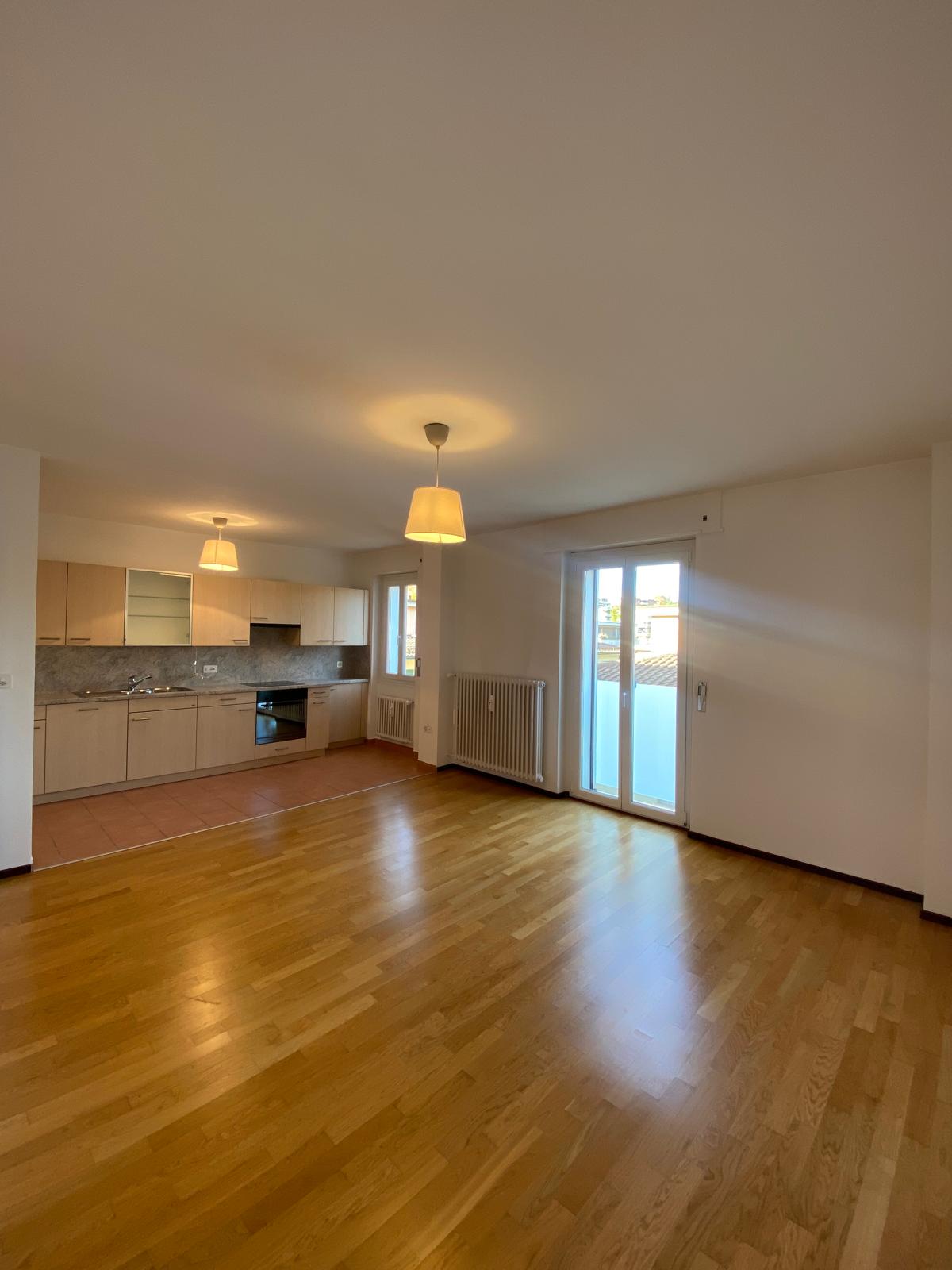 Empty room, open kitchen, wooden floor, white walls, two sliding doors, radiator, modern kitchen with black stove and kitchen island.