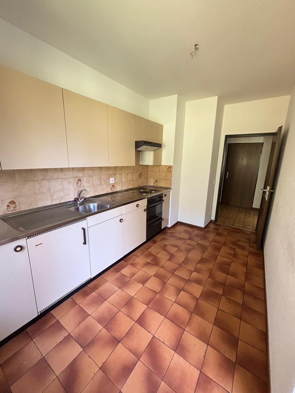 Modern kitchen with white cabinets, tiled countertops, stainless steel sink, and appliances. Brown tiled flooring.