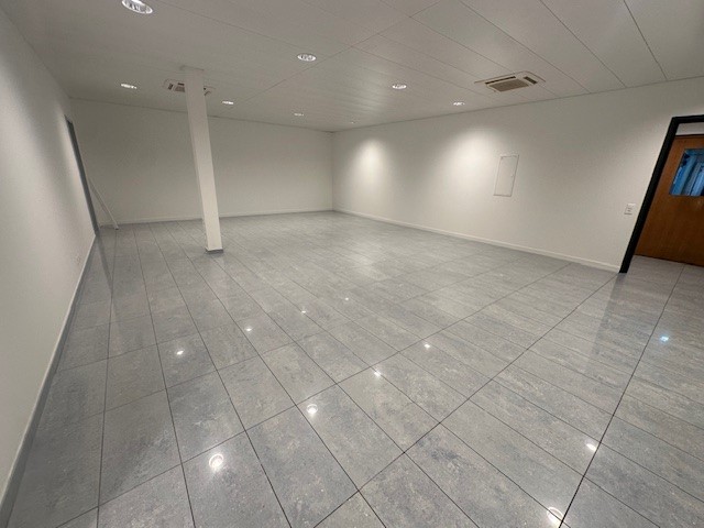 white walls, gray floor tiles, column in the middle, white ceiling, lights on the ceiling, empty room
