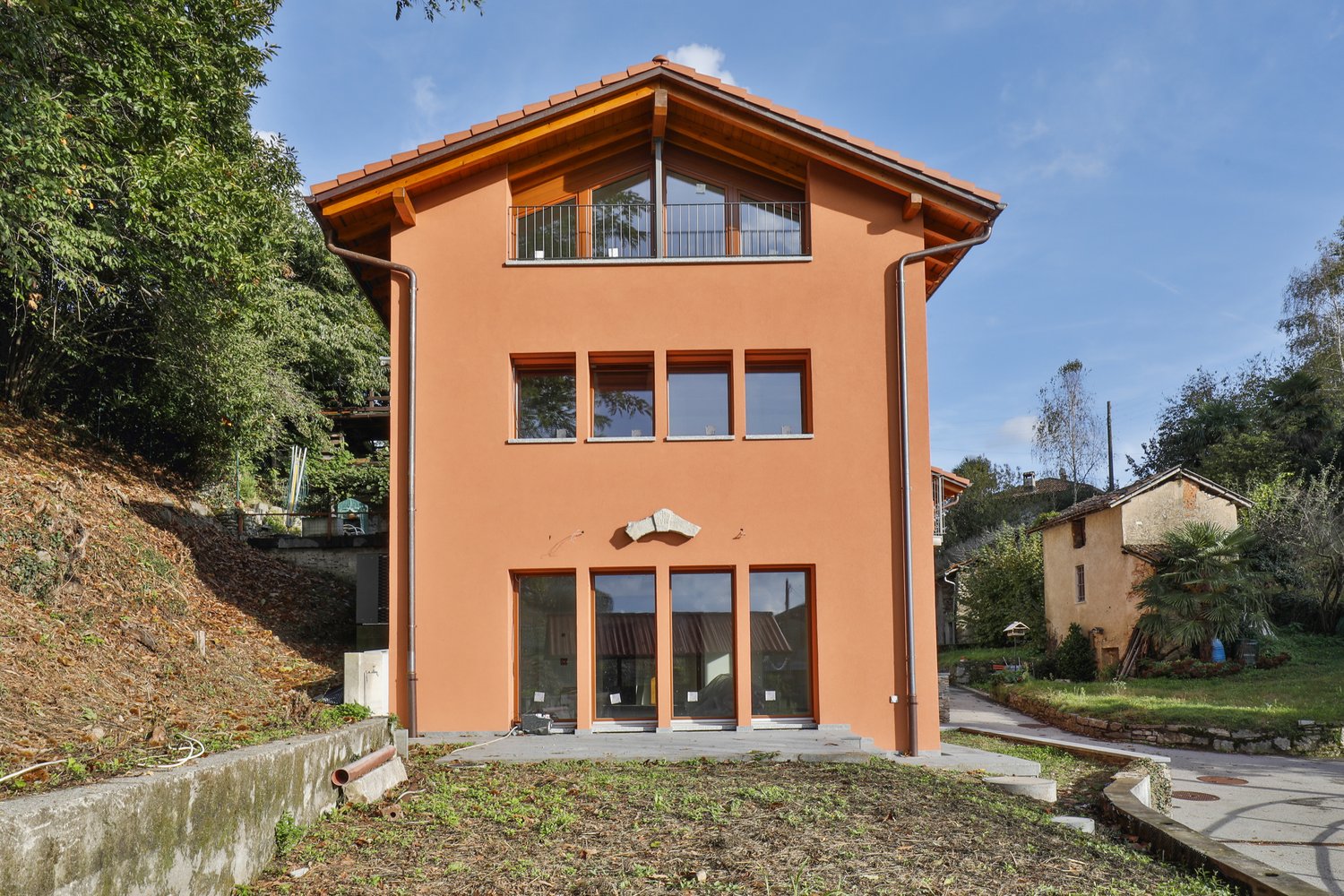 Two-story house, bright orange exterior, multiple large windows, black railing on balcony, located on a hillside