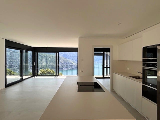 Spacious open-plan living area with large windows offering a scenic view, modern kitchen with built-in appliances, and access to a balcony or terrace