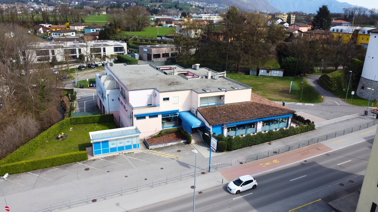 modern building with multiple floors, multiple windows, car in the parking lot, paved area, trees