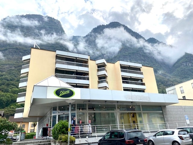 A multi-story commercial building with a parking lot in front, located in a mountainous area with clouds and fog in the background.