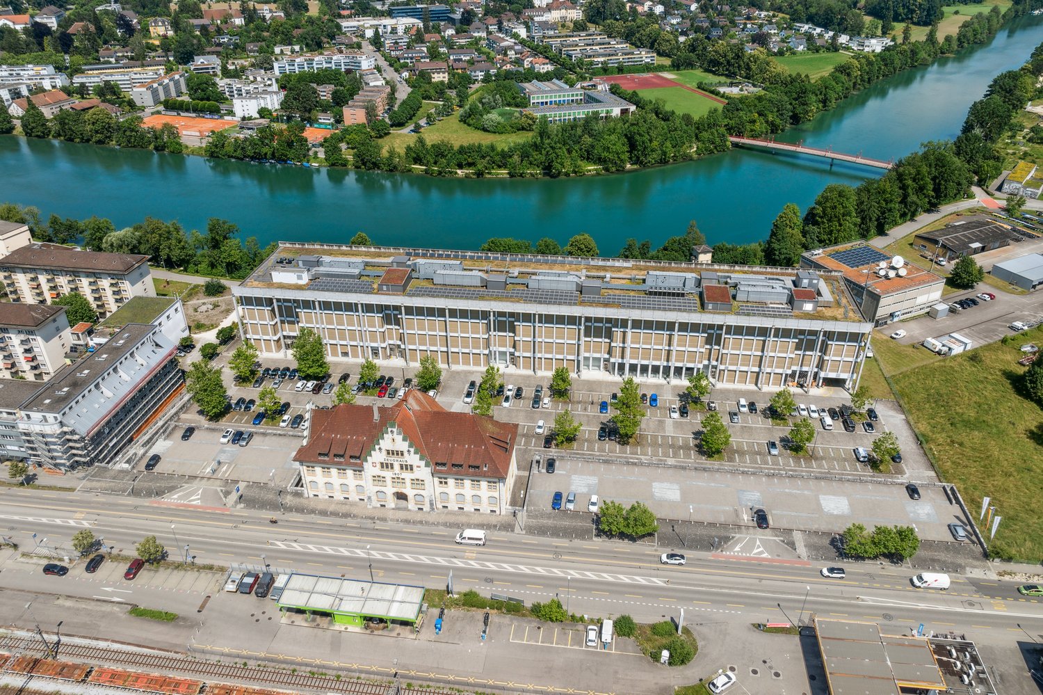 Aerial view of a large commercial building with a parking area and several other buildings along the river.