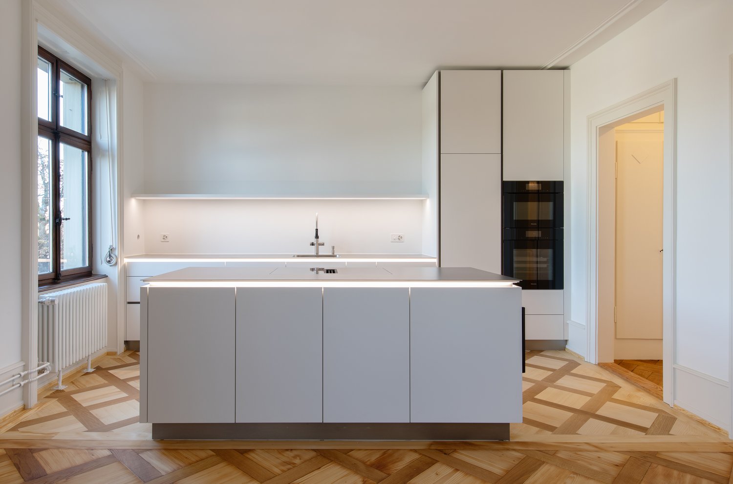 modern kitchen with white cabinets, central island, sink, oven, wooden floor, window