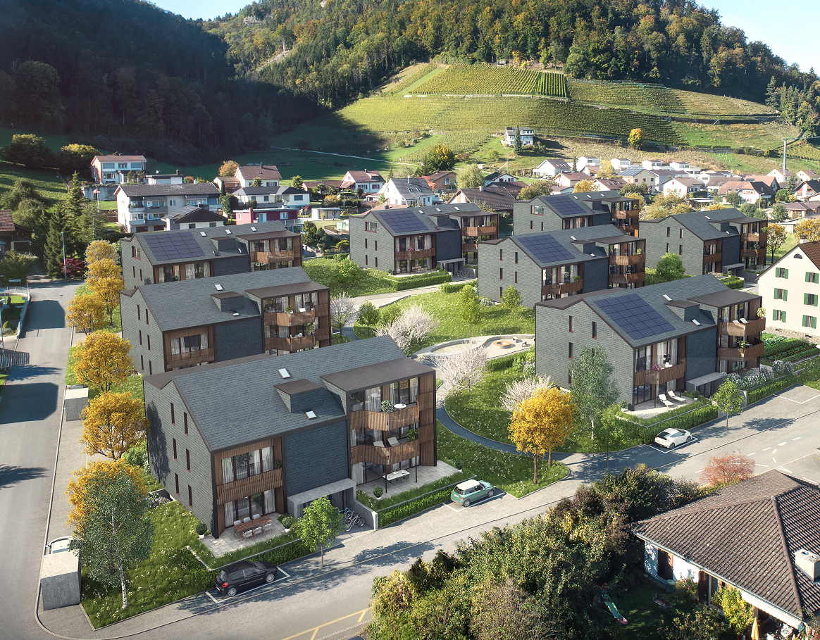 Aerial view of a residential area with multi-story apartment buildings, surrounded by lush greenery and vineyards on the hills in the background.