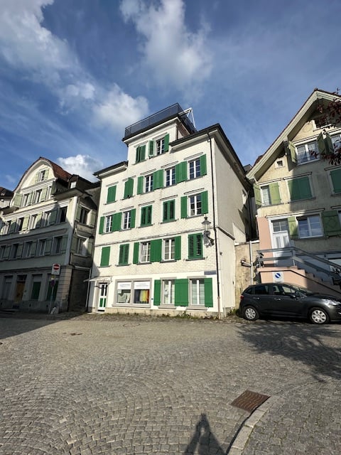 3 story building, white exterior, green shutters, cobblestone street, parked car