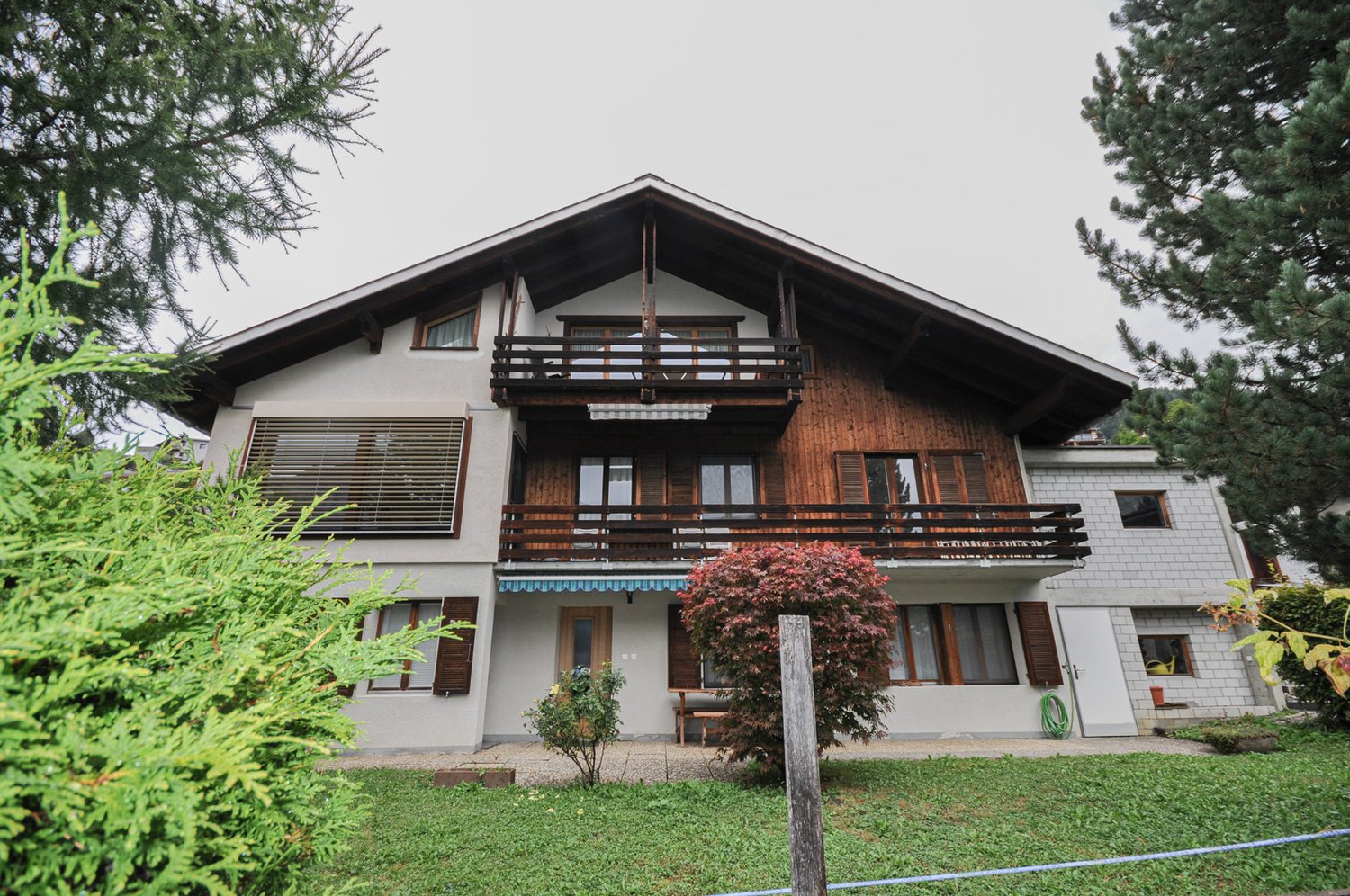 2 story house, wooden trim, white walls, balcony, shrubs, garden, and a tree in front