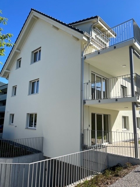 3-story apartment building with white exterior, black roof tiles, and balconies on the upper floors.