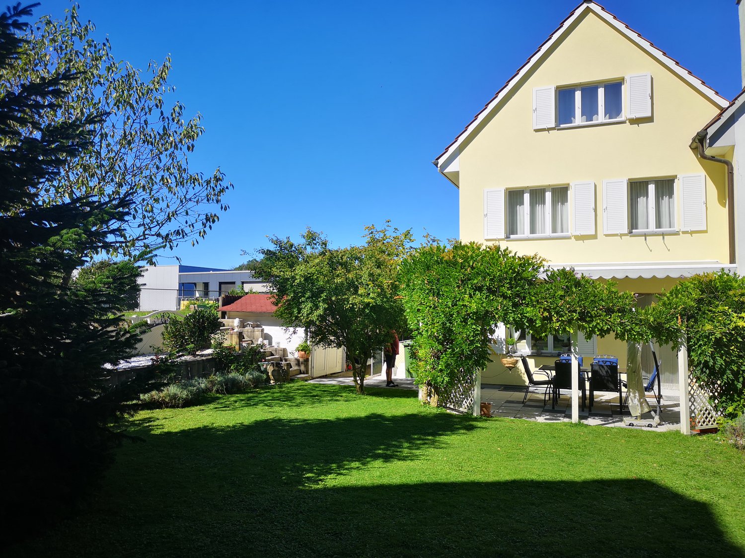 yellow house with white trim, patio, trees, lawn, and a view of a mountain