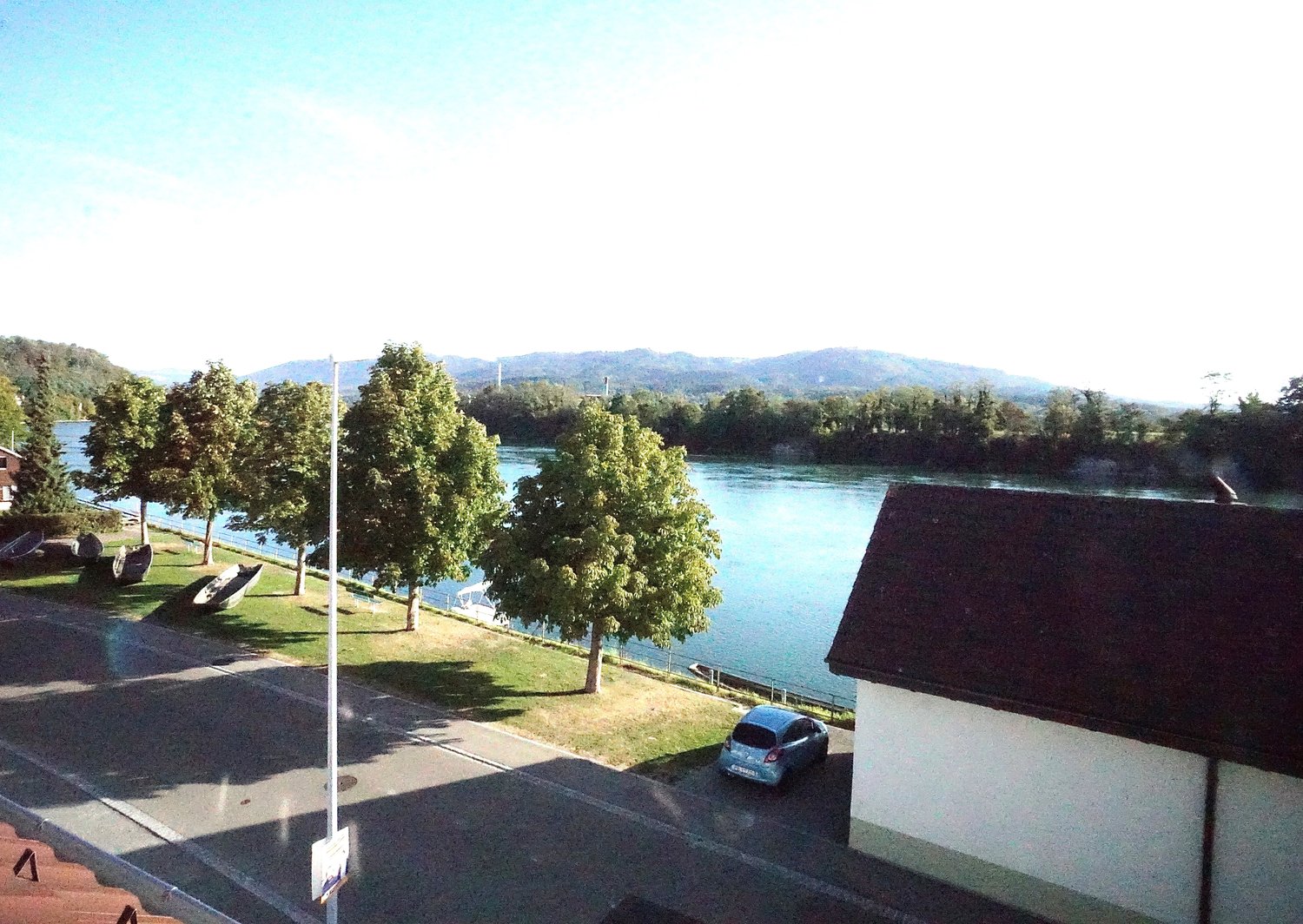 Building with a view of the river, a blue car is parked in front