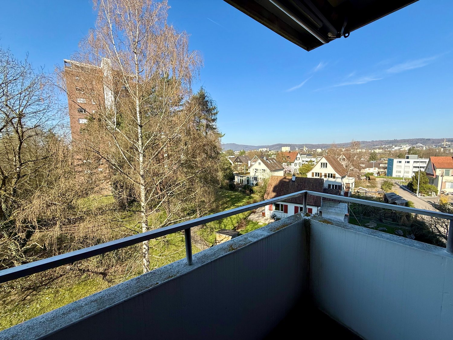 balcony with metal railing, overlooking a grassy area with trees and a building