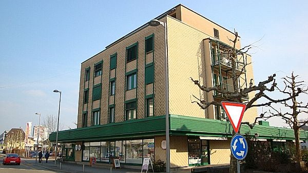 5 story building, brown walls, green roof, shops on ground floor, windows with shutters