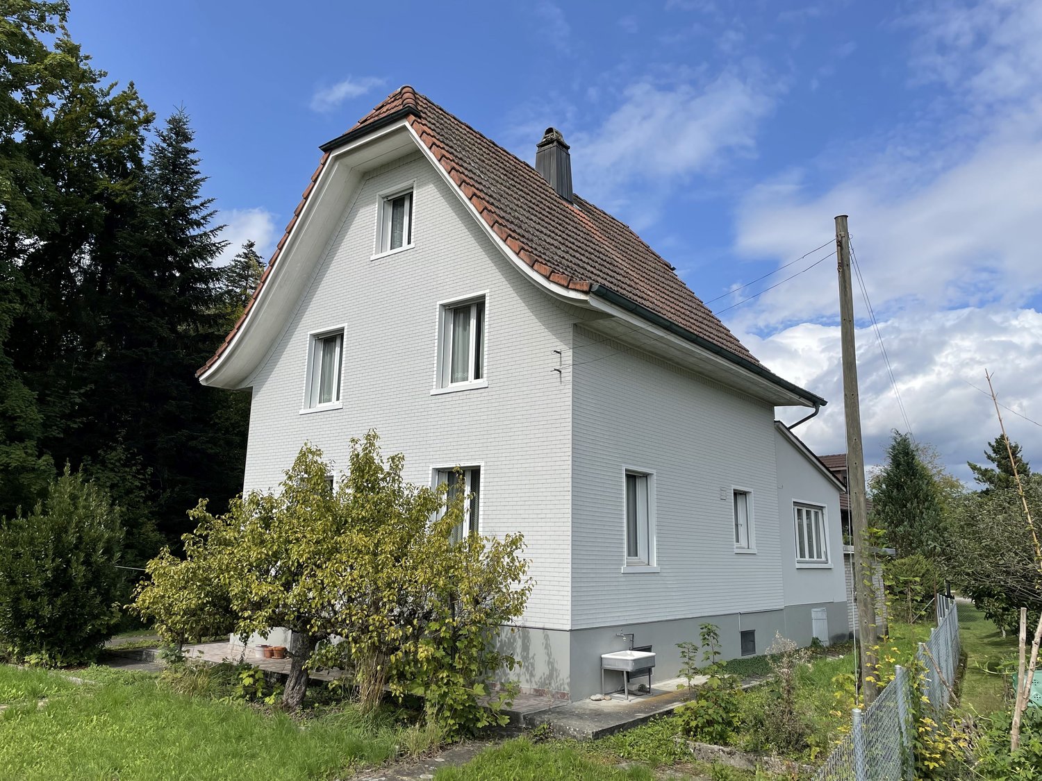 2 story house, white exterior, brown roof, large windows, front yard with greenery