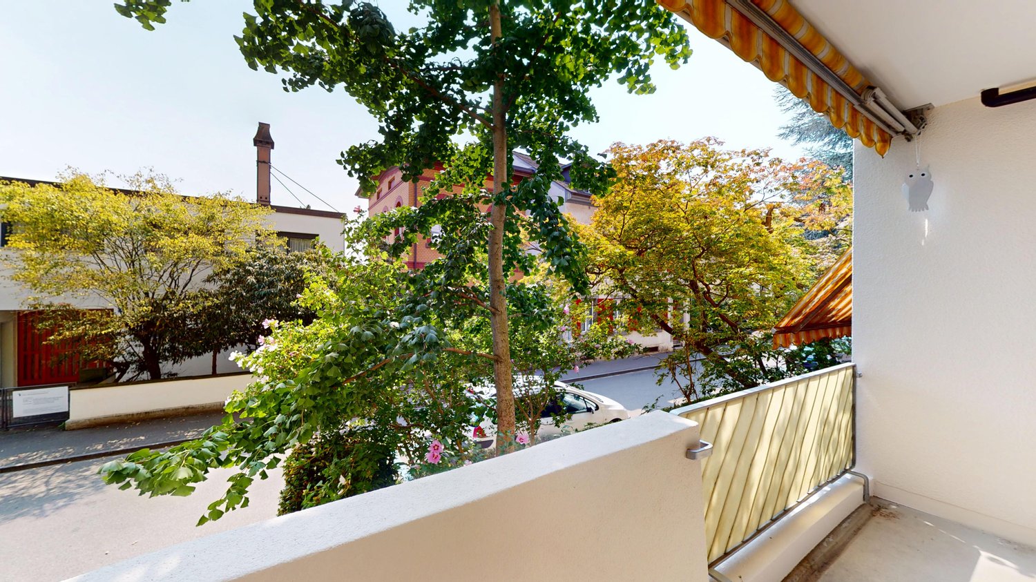 Tree-lined street, yellow leaves, balcony, metal railing, orange striped awning