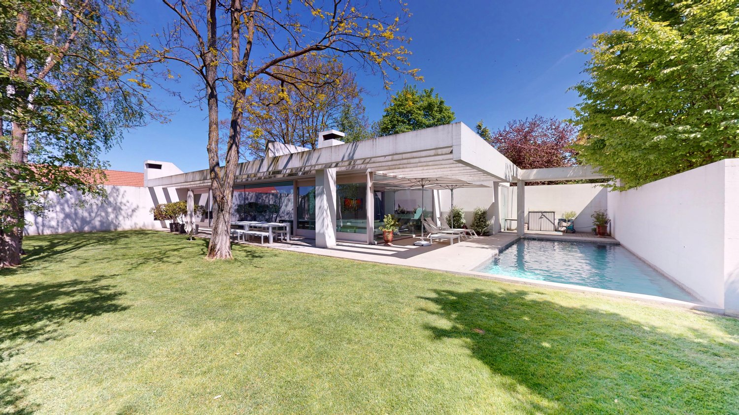 Modern house, white exterior, large windows, outdoor dining area, swimming pool, garden, trees