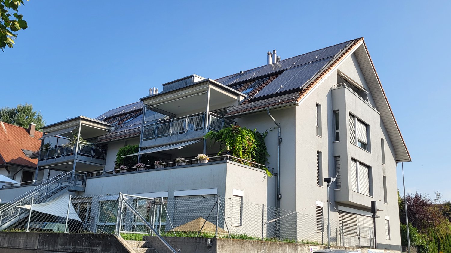2 story house, solar panels on roof, multiple balconies, fenced yard, greenery in foreground