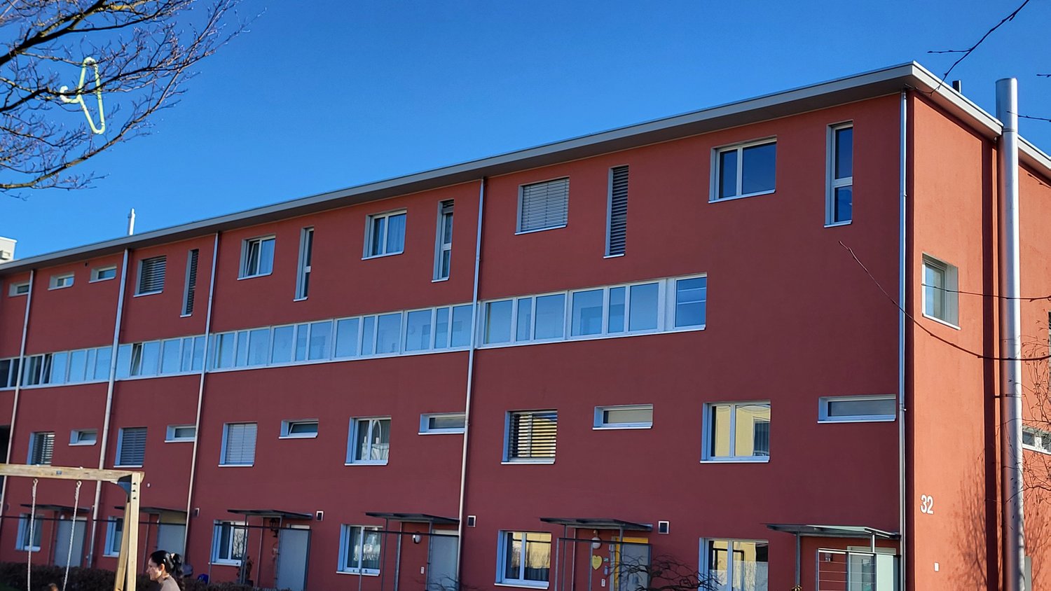 Red building with multiple windows, multiple floors, entrance with awning, number 32 on the right side